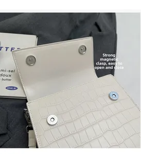 Detail view of the white crocodile-embossed bag featuring four strong magnetic buckles
