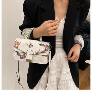 Detail der Blumen- und Schmetterlingsstickerei auf weißer Tasche mit goldenem Verschluss