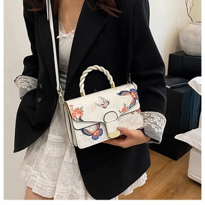 Detail einer weißen PU-Handtasche mit Schmetterlings- und Blumenmuster zum schwarzen Blazer