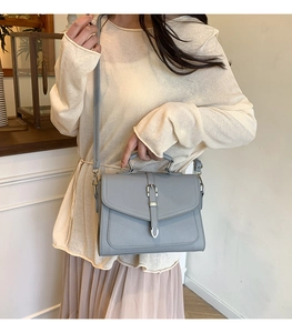 Blue faux leather handbag with silver buckle shown styled with a knit sweater