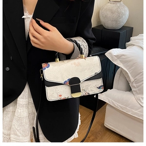 Detail der weißen Handtasche mit Blumenmuster, schwarzem Kontrast und Goldschnalle