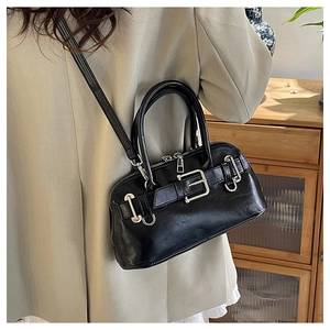 Detail of a black glossy leather shell bag with silver buckle and adjustable shoulder strap