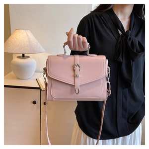 Pink crossbody bag with metal buckle shown in a lifestyle home setting by a model