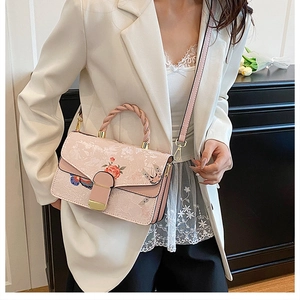 Detail einer hellrosa Handtasche mit elegantem Blumenmuster und goldenen Beschlägen