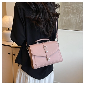 Pink faux leather crossbody bag with silver buckle worn by a model in a modern room