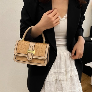 Elegant cream lace crossbody bag with gold hardware worn by a model in a black suit