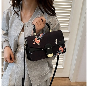Detail der schwarzen Handtasche mit orangefarbenen Blumen und Metallverschluss am Gurt
