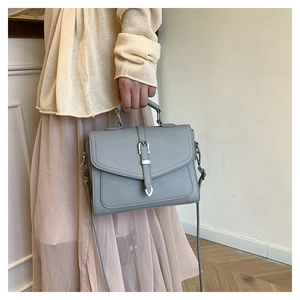 Close-up of grey leather crossbody bag with metallic buckle detail and slim strap