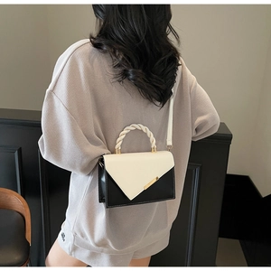 Model wearing a modern black and white color block crossbody bag with gold metal trim