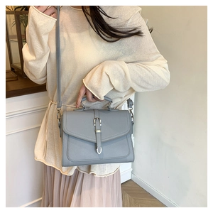 Light gray faux leather crossbody bag with silver buckle worn by a model in a minimal setting