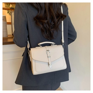 Beige faux leather shoulder bag with buckle detail worn by a model in a cafe setting