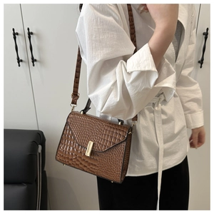 Détail d'un sac bandoulière marron effet crocodile avec boucle dorée porté par un mannequin