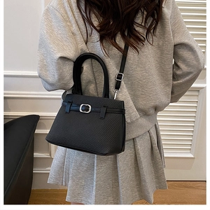 Detail of a black woven tote bag with silver buckle worn by a model in a minimalist setting