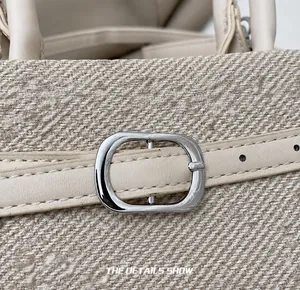Detail of silver metal buckle and beige leather adjustable strap on woven tote bag