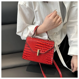 Vue détaillée d'un sac à main rouge motif crocodile avec fermoir doré porté par un mannequin