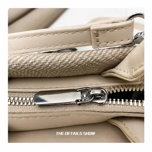 Macro view of smooth silver metal zipper and fine stitching on the beige leather handbag