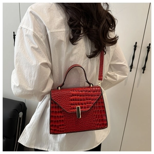 Sac carré chic rouge à texture lézard porté en bandoulière sur une chemise blanche
