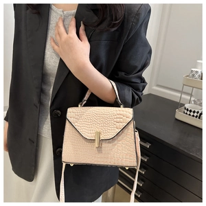 Détail du sac carré rose à motif crocodile avec boucle dorée porté par un mannequin