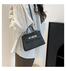 Detail of a chic black sequined crossbody bag with a gold clasp worn by a model