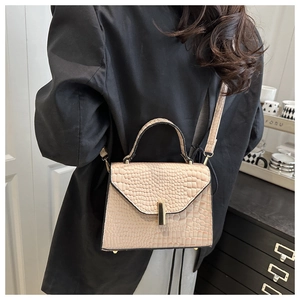 Gros plan d'un sac beige motif crocodile avec fermoir doré sur mannequin en noir