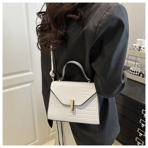 Détail d'un sac à main blanc motif crocodile avec fermoir doré et bandoulière porté par un modèle