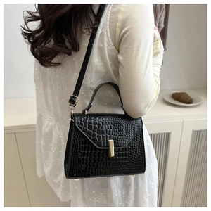 Détails d'un sac bandoulière noir à motif crocodile porté par un mannequin