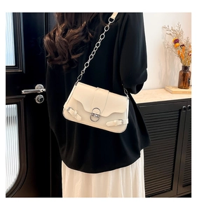 Détail d'un sac bandoulière crème avec boucle argentée et chaîne porté sur modèle