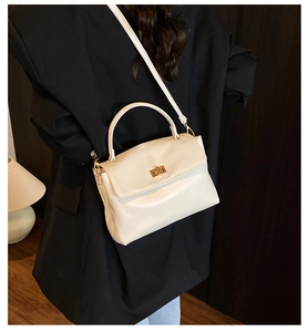 Detail of soft cream leather crossbody bag with golden clasp worn with a black blazer