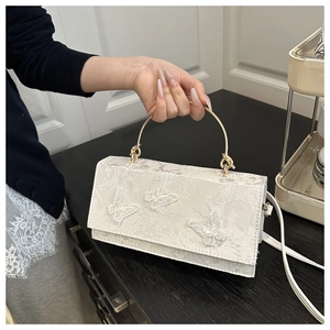 Detail of white lace butterfly embroidery on a handbag with golden round handles