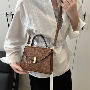 Sac à main marron texture crocodile avec fermoir doré porté par un mannequin pour l'échelle