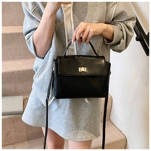 Close-up of black crossbody bag with gold buckle on a stylish model in street setting
