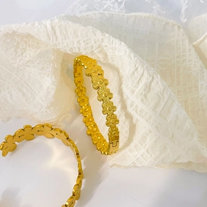 Detailed macro view of 18K gold plated flower pattern bangles on white lace fabric