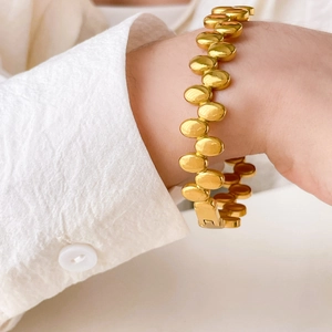 Close-up of polished 18K gold-plated oval link bracelet on a woman wrist with white shirt