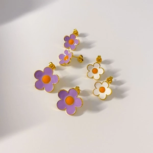 Détail macro de boucles d'oreilles fleurs en émail avec pétales violets et blancs dorés