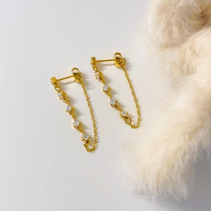 Détail de boucles d'oreilles dorées 18K avec zircons blancs et fines chaînes