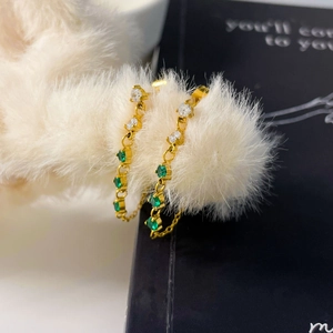 Gros plan boucles d'oreilles chaînes dorées avec zircons verts et blancs sur fourrure