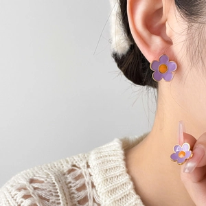 Détail de puce d'oreille fleur violette avec cœur orange sur mannequin en pull blanc