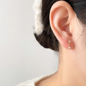 Gros plan de boucles d'oreilles minimalistes en or avec deux zircons clairs portées
