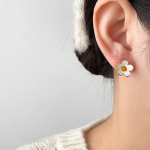 Détail de boucles d'oreilles marguerites blanches et dorées sur le lobe d'une femme