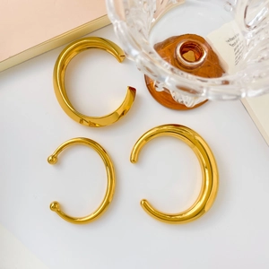 Detailed view of three polished 18K gold-plated stainless steel open bangles on a desk