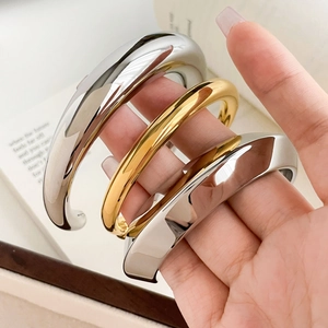 Polished chunky gold and silver C-shaped bangles held in hand for a minimalist luxury look