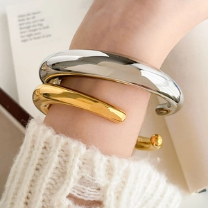 Detail of chunky hollow geometric bangles in gold and silver finish on knit sweater