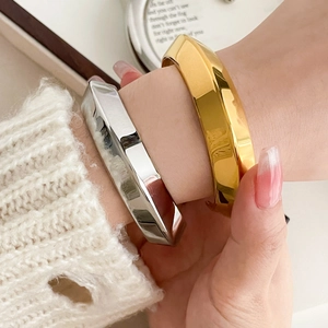 Close-up of gold and silver hollow geometric bangles on a white knit sweater cuff