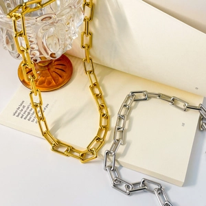 Close-up of gold and silver paperclip link necklaces on a book and glass decor