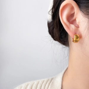 Macro side view of an 18K gold-plated C-shape wave earring worn on the earlobe