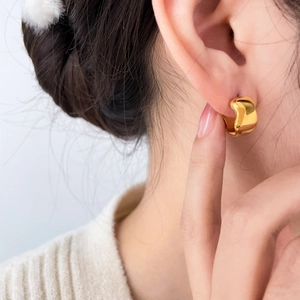 Macro side view of a wide C-shaped wavy gold earring worn on a model ear lobe