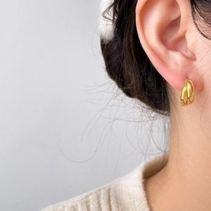 Close-up of golden teardrop earring with wave geometry on ear for detailed texture view