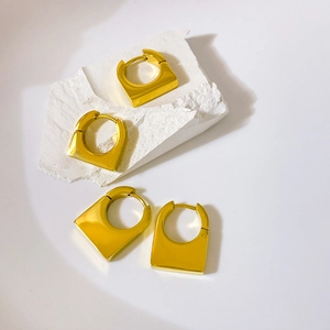 Macro detail of polished gold geometric D-shape hoop earrings on white stone props