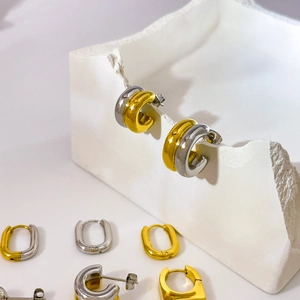 Detail of two-tone C-shaped hoop earrings on white stone display block