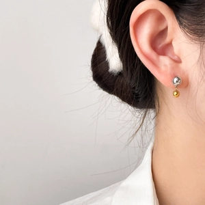 Close-up of minimalist two-tone steel stud earrings with gold and silver spheres